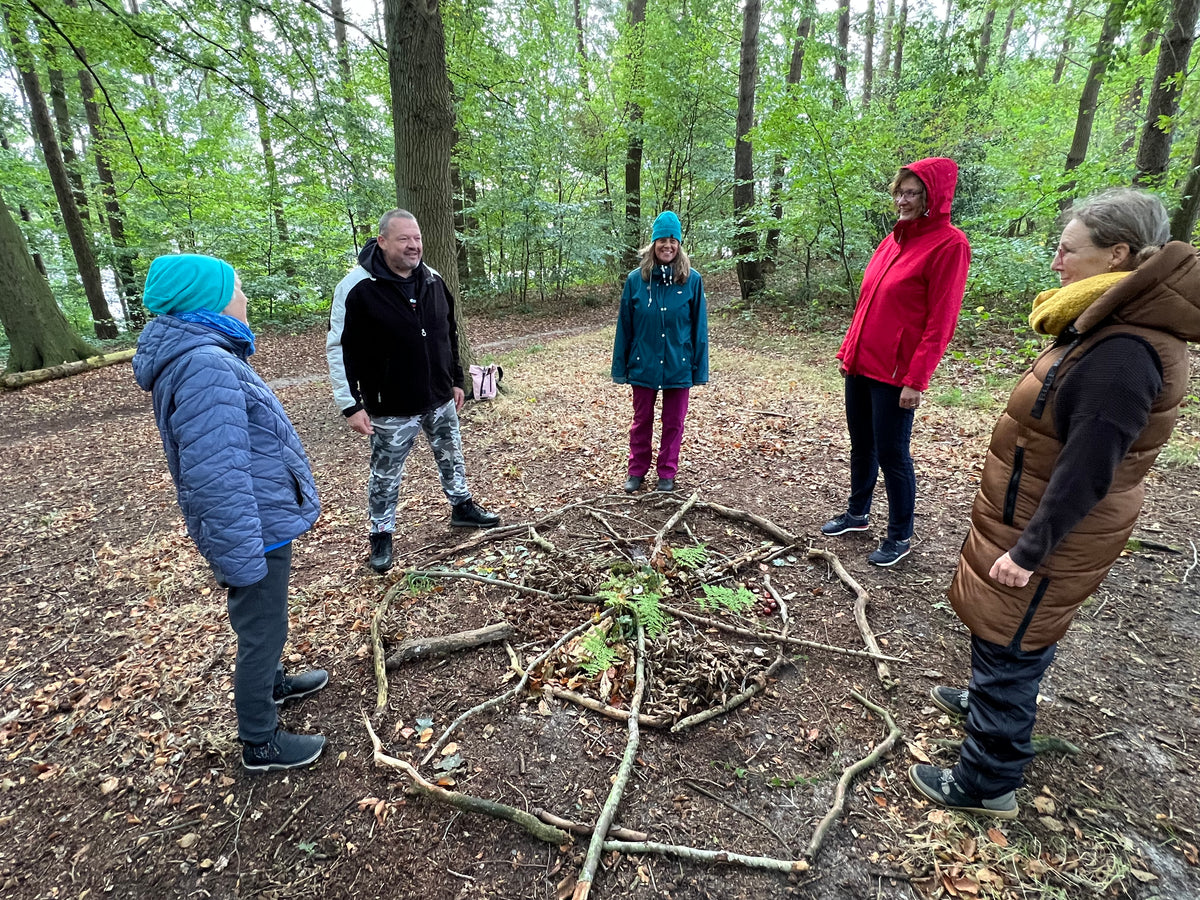 Eine Gruppe beim Waldbaden rund um ein Mandala aus Naturmaterialien